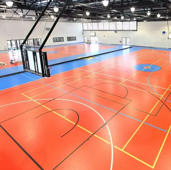 Kapalı spor salonunda kiremit ve mavi PVC zemin, çok branşlı saha çizgileri ve basketbol potası